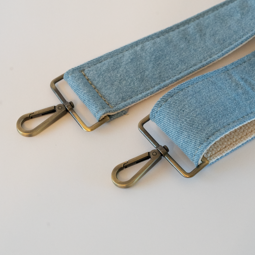 Denim strap with brass hardware on a light gray background